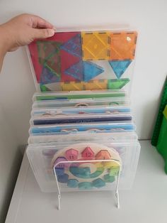 a stack of plastic storage containers filled with different colored shapes and sizes on top of a white table