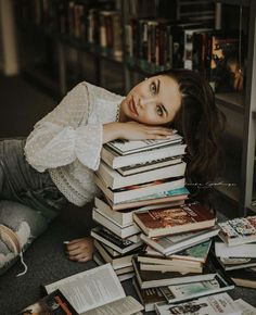 a woman is laying on the floor next to a pile of books and looking at the camera