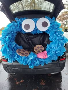 the trunk of a car decorated with blue and black paper pom poms, googly eyes and a cookie on it