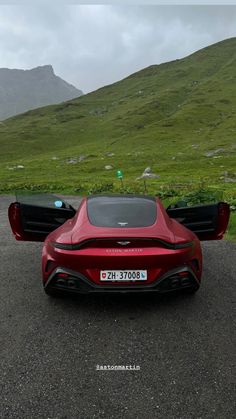 two red sports cars parked on the side of a road in front of green mountains