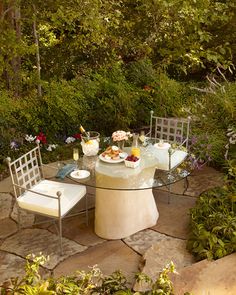 an outdoor table with chairs and plates on it in the middle of a garden area