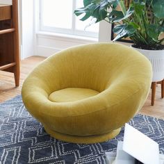 a yellow chair sitting on top of a blue rug next to a potted plant