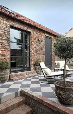 an outdoor patio with chairs and a potted tree in front of a brick building