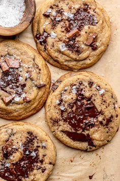 four chocolate chip cookies on top of a piece of parchment paper next to a wooden spoon