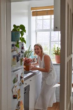 a woman standing in a kitchen next to a sink and dishwasher with plants on the counter