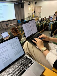 two people sitting in front of laptops on their lap tops while others look at them