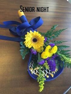 a blue vase filled with yellow and purple flowers on top of a wooden table next to a ribbon