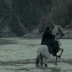 a man riding on the back of a white horse across a river