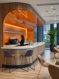 a woman is sitting at the bar in an office setting with chairs and tables around it