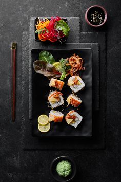 sushi is served on a black plate with chopsticks next to the dish