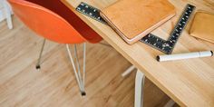 a wooden table topped with a notebook and ruler next to an orange chair on top of a hard wood floor