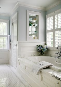 a white bath tub sitting next to a window filled with shuttered glass doors in a bathroom