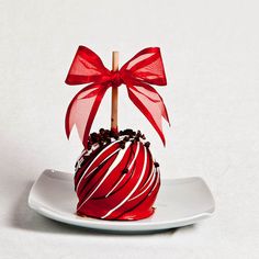 a red and white striped chocolate covered apple on a plate with a wooden stick sticking out of it