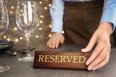 a person with their hand on a reserved sign next to some wine glasses and candles