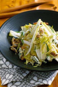 a black plate topped with shaved vegetables on top of a wooden table next to utensils