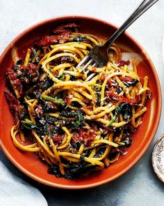 an orange bowl filled with pasta and spinach