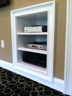 there is a shelf with some electronics on it in the corner by the wall and carpet