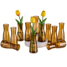 a group of vases with flowers in them on a white table top and one has yellow tulips growing out of it