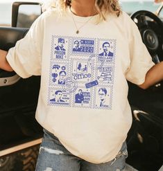 a woman standing in front of a car wearing a white shirt with blue images on it