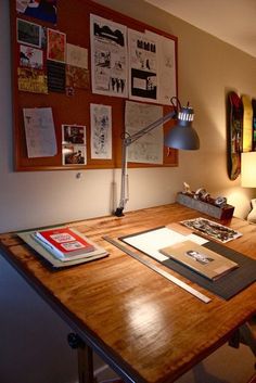 a wooden desk topped with books and a lamp next to a wall covered in pictures