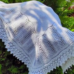 a white crocheted shawl sitting on top of a lush green forest covered in leaves