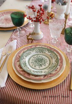 the table is set with plates, silverware and red striped napkins on it