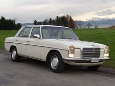 an old white car is parked on the side of the road in front of some grass