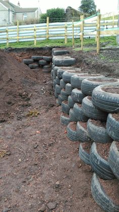 a pile of old tires sitting on top of a dirt field next to a fence