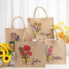 three jute bags with flowers on them sitting next to sunflowers and a basket