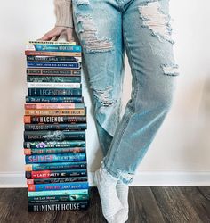 a woman holding a stack of books in her hand and leaning on the wall behind her