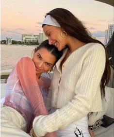 two women sitting on the back of a boat in front of some water and buildings