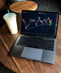 a laptop computer sitting on top of a wooden table next to a cup of coffee