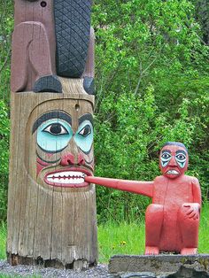 two totems with faces painted on them pointing at each other in front of some trees