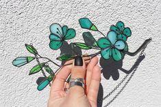 a hand holding a piece of stained glass with green leaves on it, next to a chain