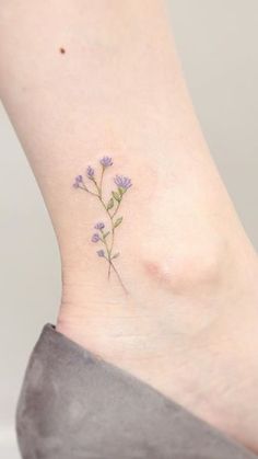 a small flower tattoo on the ankle that is purple and has green leaves growing out of it