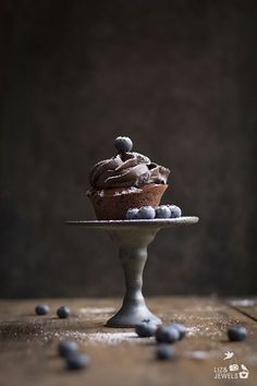 a chocolate cupcake sitting on top of a cake plate with blueberries around it