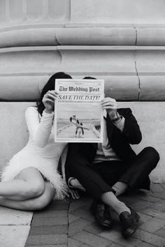 a man and woman sitting on the ground reading a newspaper