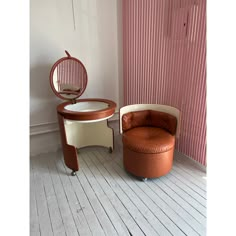 an orange chair sitting next to a round mirror on top of a wooden floor in front of a pink wall