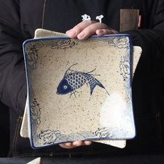 a person holding a plate with a fish design on the front and side, in their hands