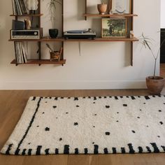 a white rug with black dots on it in front of a wall mounted bookshelf