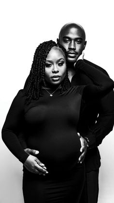 a man and woman standing next to each other in front of a white wall with their hands on the pregnant belly