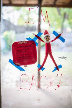 an elf is holding a red suitcase in front of a sign that says i'm back