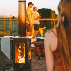 two people standing next to an outdoor wood burning stove