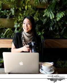 a woman sitting at a table with a laptop and coffee in front of her smiling