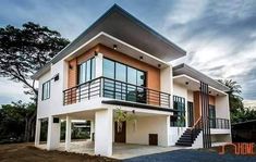 a two story house with white walls and black railings on the second floor, surrounded by trees