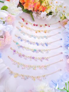 a bunch of flowers that are next to some necklaces on a white surface with pink and blue flowers in the background