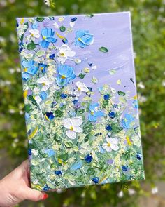 a person holding up a piece of art with blue flowers painted on it and green grass in the background