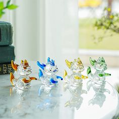 four glass figurines sitting on top of a white table next to a book