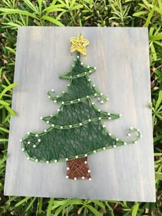 a christmas tree made out of string and beads on a piece of wood in the grass