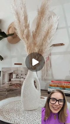 a woman sitting in front of a vase with feathers on it